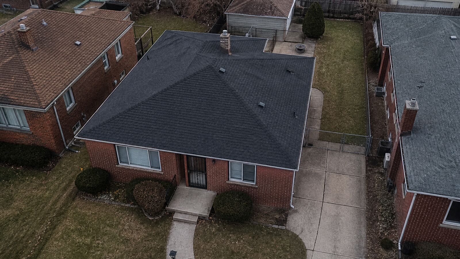 Brick house roof, driveway, and yard from a listing altitude.